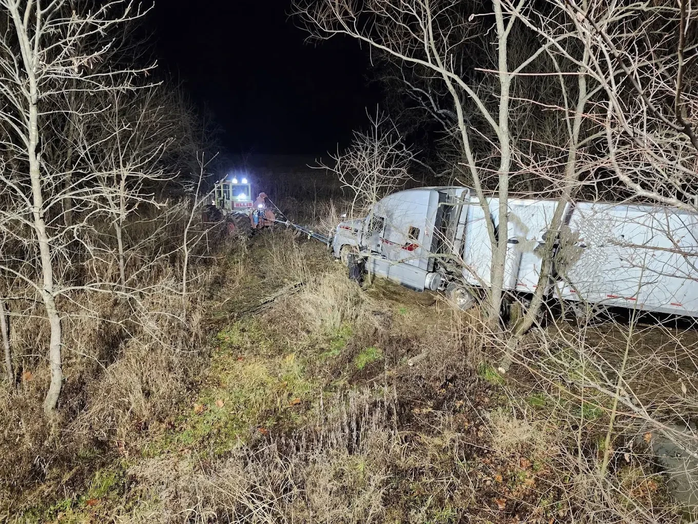 Burrows recovering a truck and trailer from a wooded ditch at night